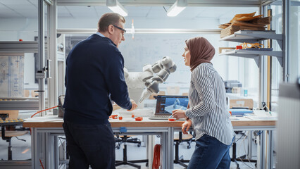 Chief Male Engineer Chatting with Arabic Female Computer Science Specialist While Standing Next to the Table with Robotic Hand. Promising Engineering Majors Collaboration Concept. Medium Shot.