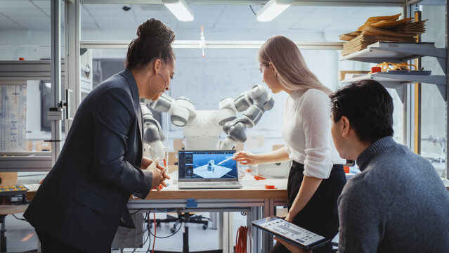 Diverse Team: Chief Engineer and Promising Computer Scientists Analyse and Discuss Optimisation of Autonomous Manufacturing Facility That Creates Great Products. Laboratory with Robotic Arm.