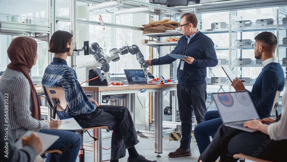 Poster male professor standing with laptop and explaining to diverse students controls of robotic hand. hig