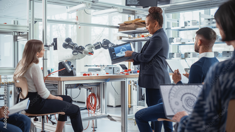 Poster Enthusiastic Black Female Chief Engineer Explains to Computer Scientists and Developers Principles of Robotic Arm Controls. Young Intelligent People Acquire New Technical Information.
