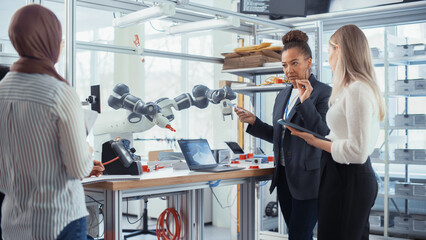 Black Senior Engineer Explaining Information. People Look at Robot Limb. Interns Hold Devices and...