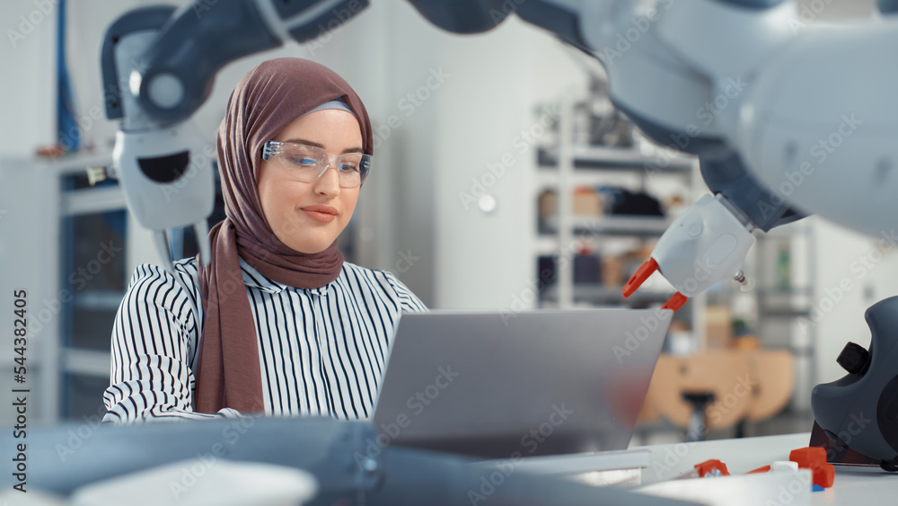 Aufkleber Middle Eastern Engineer in Hijab Conducts an In-depth Analysis of the Robot Arm and Programs on Laptop at Modern Office. Optimisation of Autonomous Manufacturing Facility For High Tech Products.