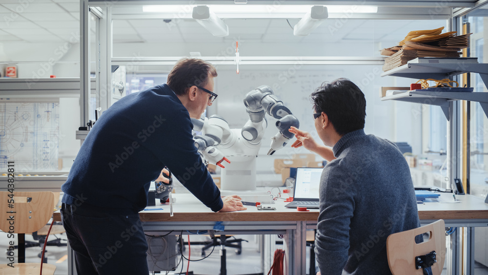 Poster Adult Engineer Changes Position of Robotic Arm with Controller and Having a Discussion with Young Asian Developer. Startup Laboratory and Innovative Technologies in Robotics Concept.