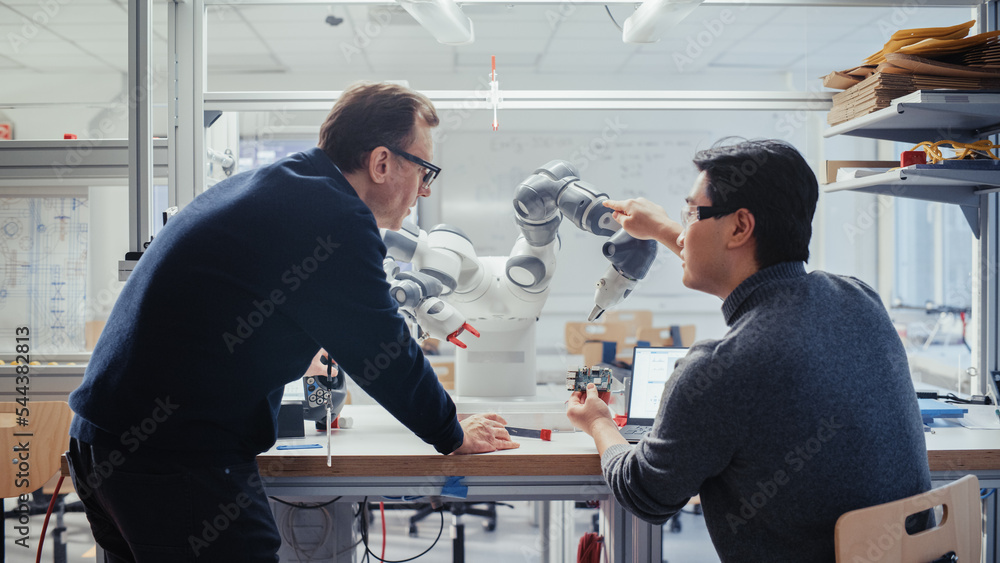 Poster Adult Caucasian Engineer Changes Position of Robotic Arm with Controller and Having a Discussion with Young Asian Developer. Startup Laboratory and Innovative Technologies in Robotics Concept.