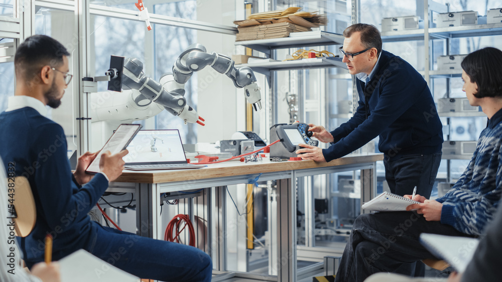 Aufkleber Chief Male Engineer Manipulates Robotic Arm and Talks with Young Computer Specialists in Factory Meeting Room, They Try to Find Problem Solutions. Developing and Robotics Industry Concept.