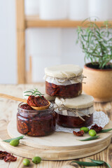 Sun-dried tomatoes with garlic, rosemary and spices in a glass jar in olive oil on wooden cutting board