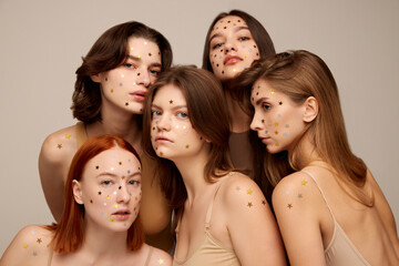 Fototapeta premium Portrait of five young beautiful women posing together in beige underwear isolated over grey background. Starry makeup