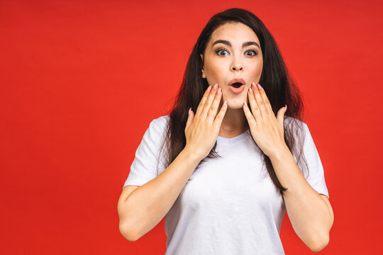 OMG! Portrait of amazed shocked surprised young woman isolated over red background.