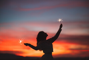 girl holding sparkler light at sunset