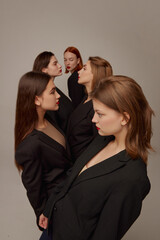 Portrait of young beautiful women in black jackets and red lipstick makeup posing over grey background. High fashion