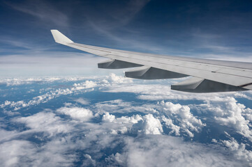 Obraz premium Wing of airplane above flat fluffy clouds surface with soft evening sunlight. Copy space.