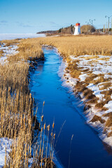 A stream running out to sea through a salt marsh with a lighthouse in the distance.
