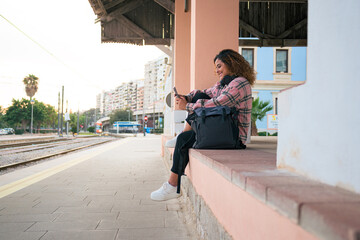 Curvy woman with curly hair looks at her phone waiting for the train