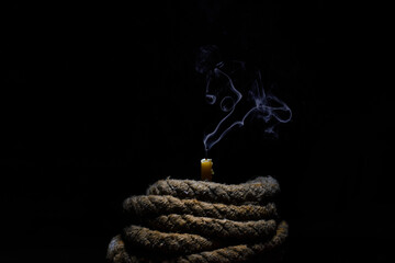 extinguished wax candle with a wick old shabby book twisted rope on a black background