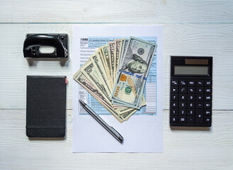 U.S. individual income tax return on a wooden table next to a calculator, dollars, money, a pen and a notepad. Blank US tax forms. View from above.