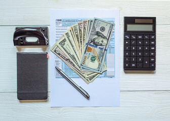 U.S. individual income tax return on a wooden table next to a calculator, dollars, money, a pen and a notepad. Blank US tax forms. View from above.