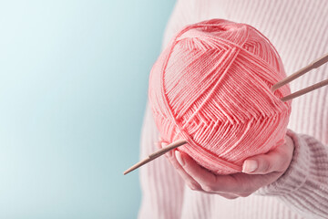 Female hands holding colorful pink wool yarns and wooden knitting needles for hobby or art work on...
