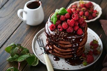 Chocolate Pancakes. Pancakes with fresh raspberry with chocolate glaze or toppings in gray bowl on old wooden table background. Homemade classic american pancakes. Page for magazine concept.
