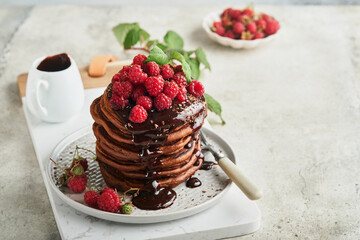 Chocolate Pancakes. Pancakes with fresh raspberry with chocolate glaze or toppings in gray bowl on light gray table background. Homemade classic american pancakes. Page for magazine concept.