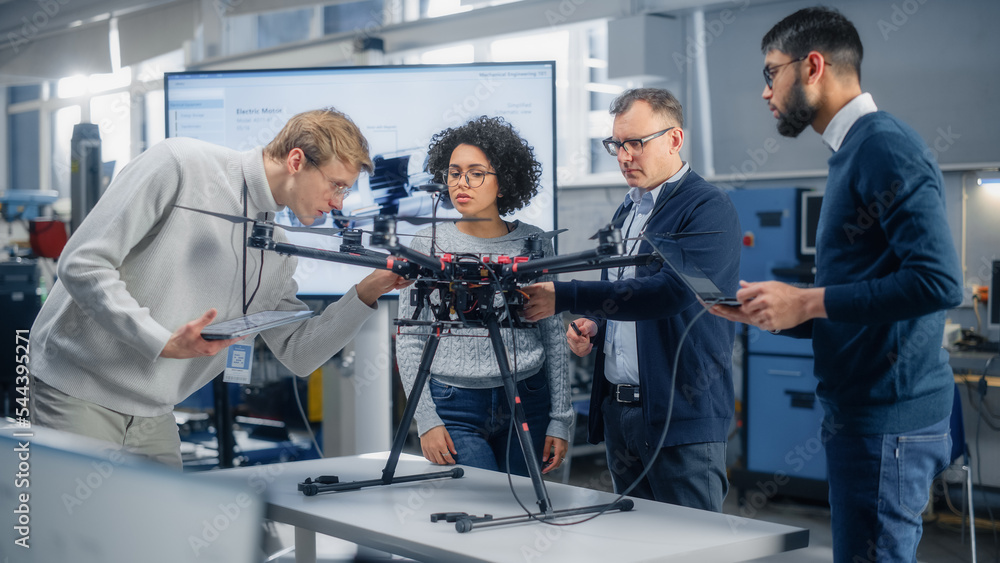 Poster team of aviation engineers work on a new drone, have discussion, use laptop in the scientific labora