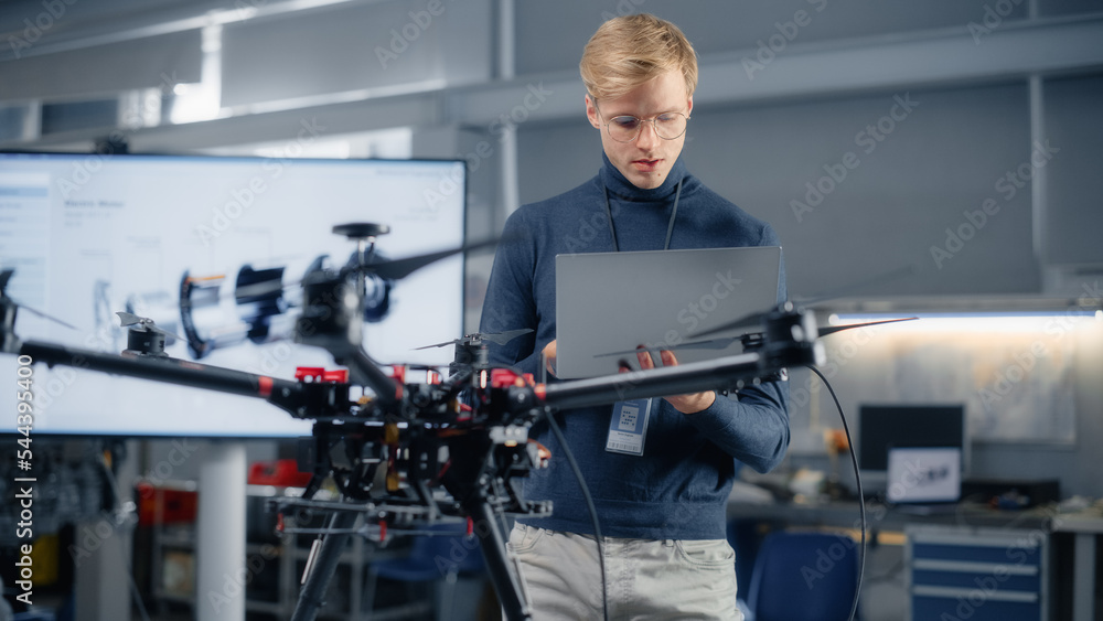 Poster Young Male Developer Programming on Laptop Computer. Working on a New Drone Design in the Research Center Laboratory. People Creating Futuristic Unmanned Aerial Vehicle Concept.