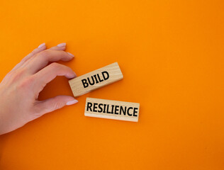 Build resilience symbol. Wooden blocks with words Build resilience. Beautiful orange background. Businessman hand. Business and Build resilience concept. Copy space.