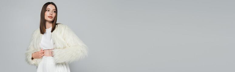 young woman in totally white outfit and trendy faux fur jacket posing isolated on grey, banner.