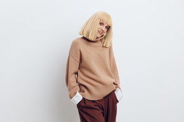 Horizontal photo, a woman on a white background in a beige sweater and brown trousers with beautiful blond hair stands and smiles