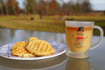 Glass Christmas coffee mug with coffee and creamer alongside a plate of chocolate chip waffles. 