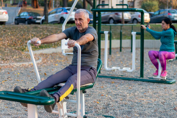 Fototapeta premium Mature man working out in the gym and leading a healthy and active lifestyle. Outdoor sports area with equipment, facilities for working out, stretching, cardio and strength physical activity.
