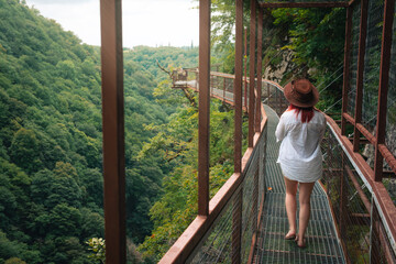 Woman traveler in Okatse Canyon in Georgia, standing on hanging metal pedestrian pathway trail...