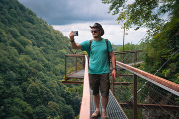 Male traveler in Okatse Canyon in Georgia, walking on hanging metal pedestrian pathway trail above...