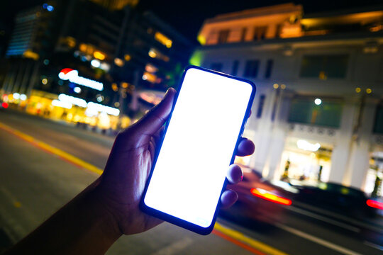 Young Man Hand Holding Smart Phone With Empty Screen At Night 