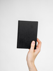 female hand holds a notebook or a book with an empty black cover. space and template for text