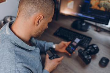 High angle of male videographer with photo camera and smartphone editing video at table with...