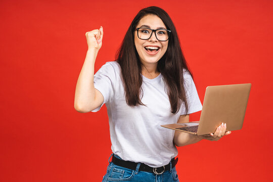 Portrait of attractive surprised excited smiling business woman using laptop computer, isolated over red background, Winner businesswoman with success