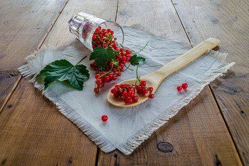 Red currants in a glass. On a wooden background, a light green napkin with leaves and red berries, on a napkin a glass transparent glass with red currant berries.