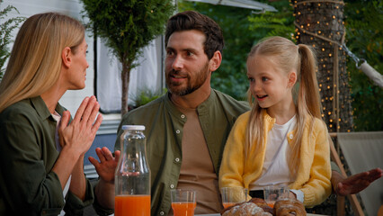 Parents with daughter have picnic with juice and croissants in camping outdoors near van. Caucasian family cheerful talking father talk story mother and child shock amaze wonder surprise fairy tale