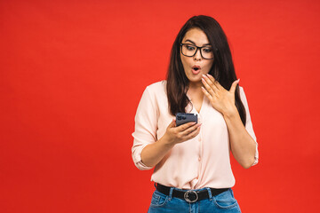 Happy winner! Portrait of surprised amazed smiling casual business woman holding smartphone isolated over red background.