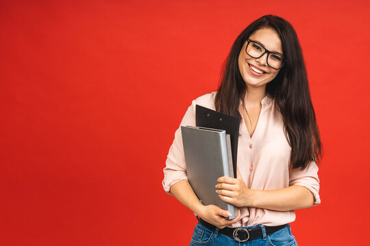 Pretty young businesswoman in casual holding laptop in the office, isolated over red background.