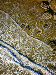 Fototapeta na wymiar Top down aerial view of waves breaking onto a sandy beach with large boulders (Southerndown)