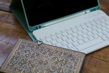 Tablet PC with keyboard, pencil and black screen and a beautiful notebook with and side closure. Material on a wooden table for remote working while traveling. Digital nomad concept.