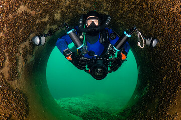 Scuba diver with a rebreather, drysuit and camera swimming through an underwater tunnel
