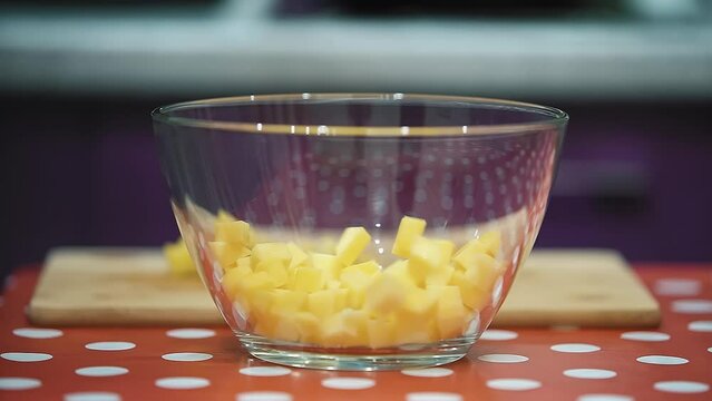 Cubes of sliced potatoes slowly fall into a transparent glass bowl. Cooking in the kitchen for the whole family. Red tablecloth with white polka dots.  Slow motion.