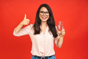 Young smiling woman holding a glass of water. Isolated studio portrait over red background.