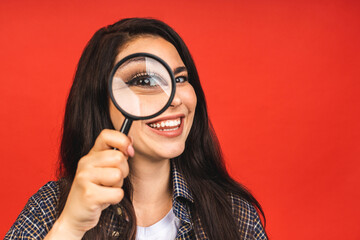 Close up portrait of amazing beautiful woman looking at camera through magnifying glass, isolated on red background. Having fun. - 544405247