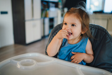 Little boy sitting in a high chair and laughing while waiting for meal. Fun family. Healthy eating. Parent, child.