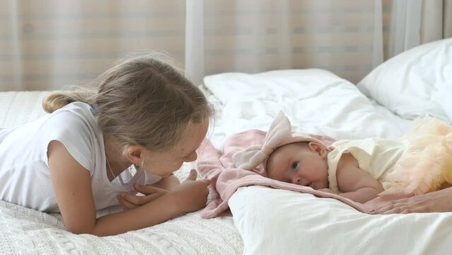 Happy little girl watching her cute baby sister lying on bed, family lifestyle concept