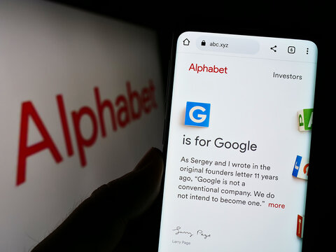 Stuttgart, Germany - 10-30-2022: Person holding cellphone with webpage of US holding company Alphabet Inc. (Google) on screen in front of logo. Focus on center of phone display.