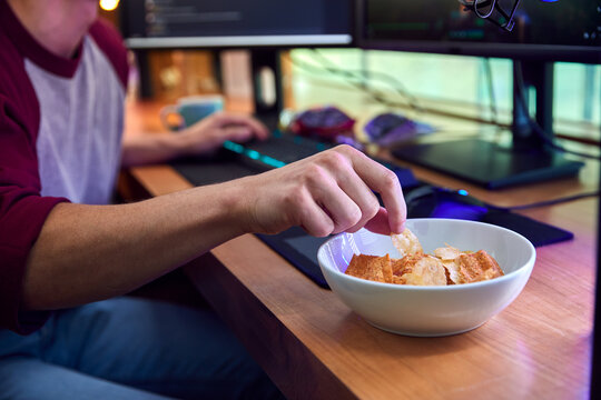 Close Up Of Man Gaming At Home Eating Potato Chips Sitting At Desk With Monitors